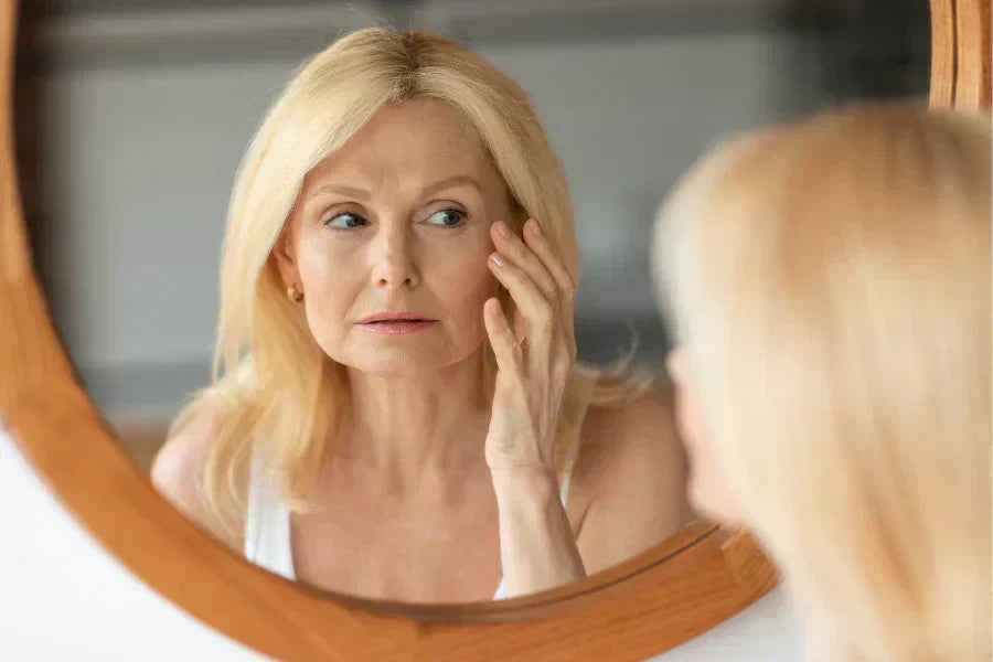 Matured women looking into the mirror, concerning on her fine lines and wrinkles