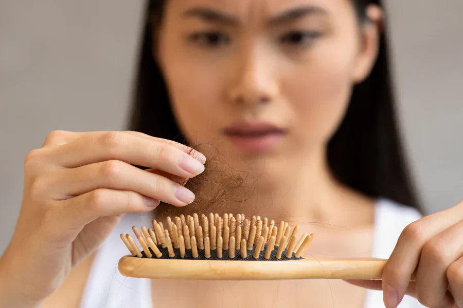 Woman looking at the amount of hair loss after combing her hair & frown
