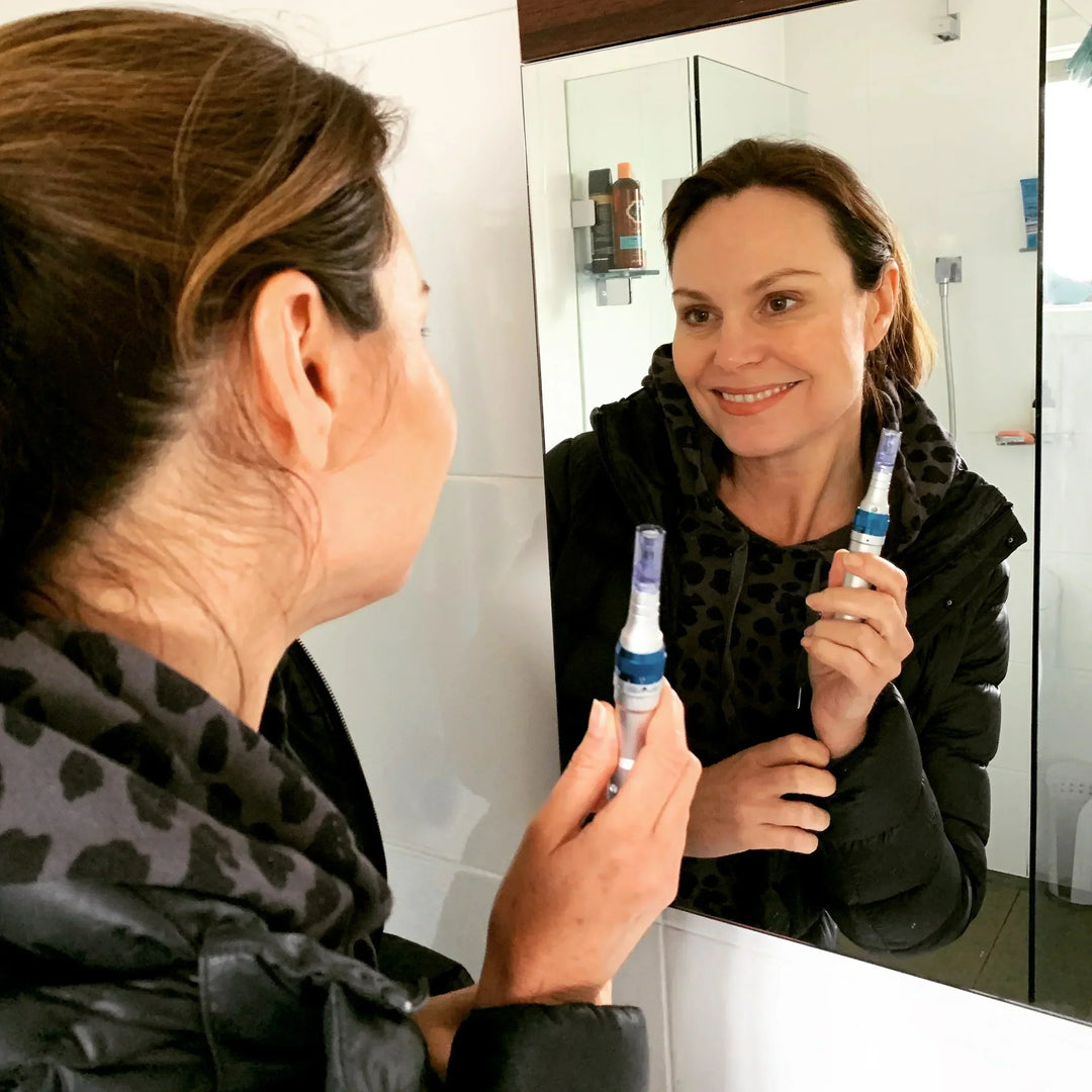 Woman smiling into the mirror with a microneedling pen