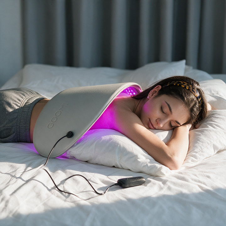 Woman using the GOOMi FlexiGlow Red Light Therapy Panel  across her back while relaxing at home