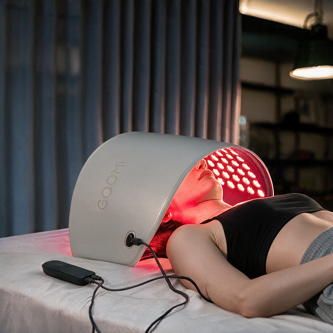 Woman using the GOOMi FlexiGlow Red Light Therapy Panel grey, angled side view with red light while lying down